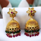 Gold earrings with red and green beads on a white cushion