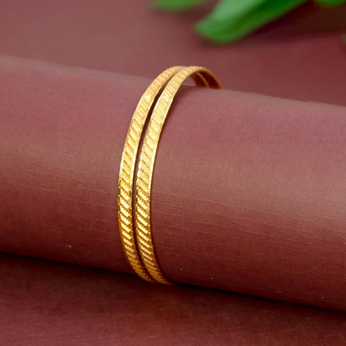 Stylish Matte Gold Plated Textured Designer Bangles on a maroon background showcasing elegant diagonal texturing.