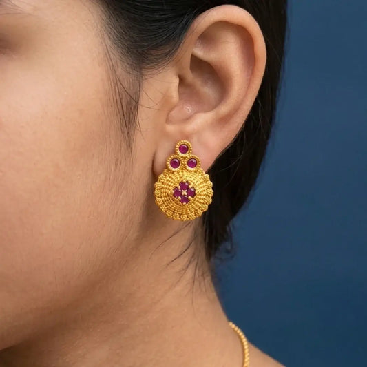 Gold Plated Floral Stone Studded Stud Earrings worn in a model's ear, featuring ruby stones and a textured gold finish.