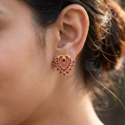 Dazzling Gold Plated Stone Heart Stud Earrings worn in an ear, showcasing layered heart design and sparkling stones.