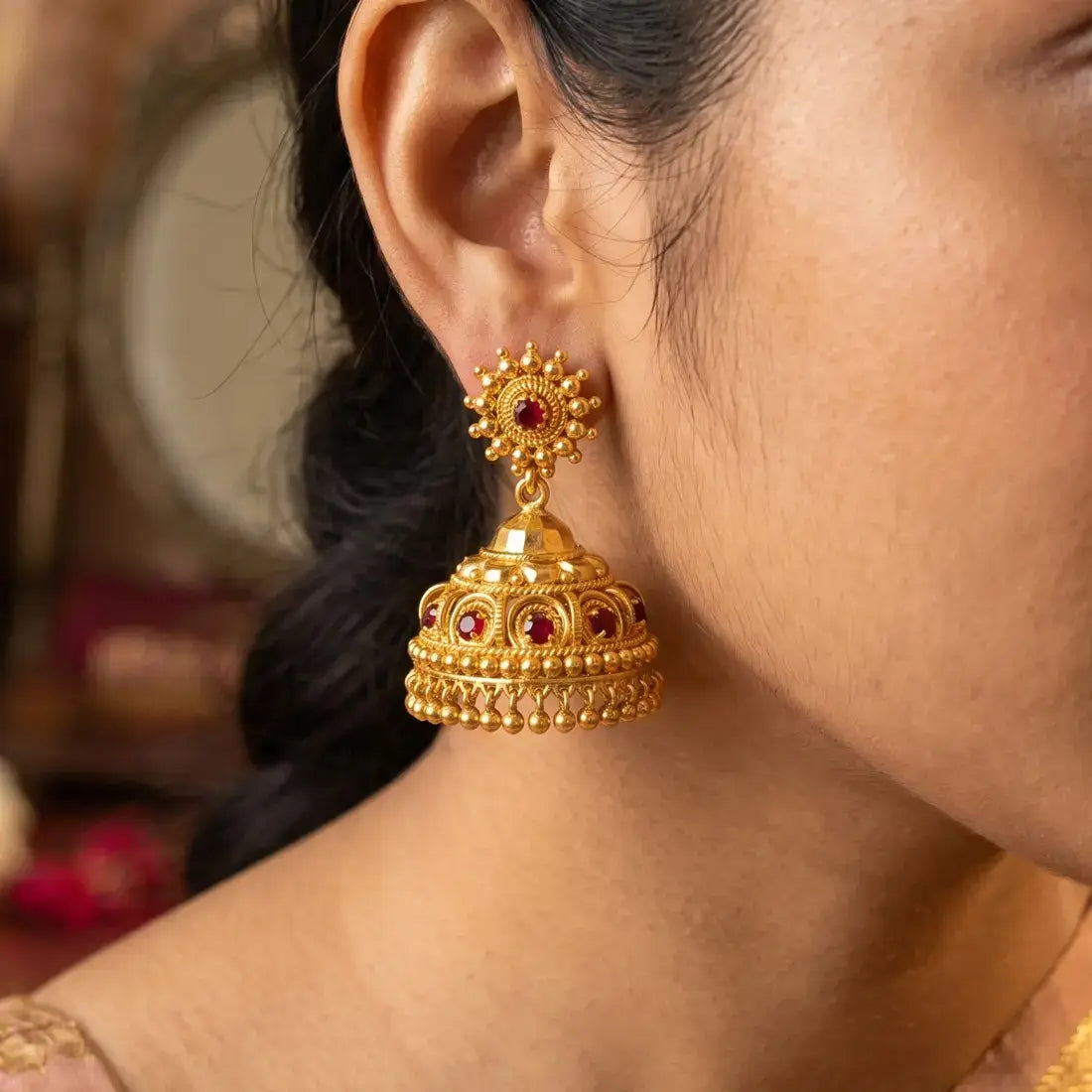 Red Stone Gold Plated Big Jhumka Earrings displayed on model, showcasing intricate design and craftsmanship.