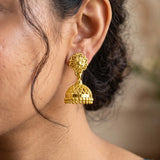 Close-up of a person wearing a gold plated jhumka earring with a blurred background
