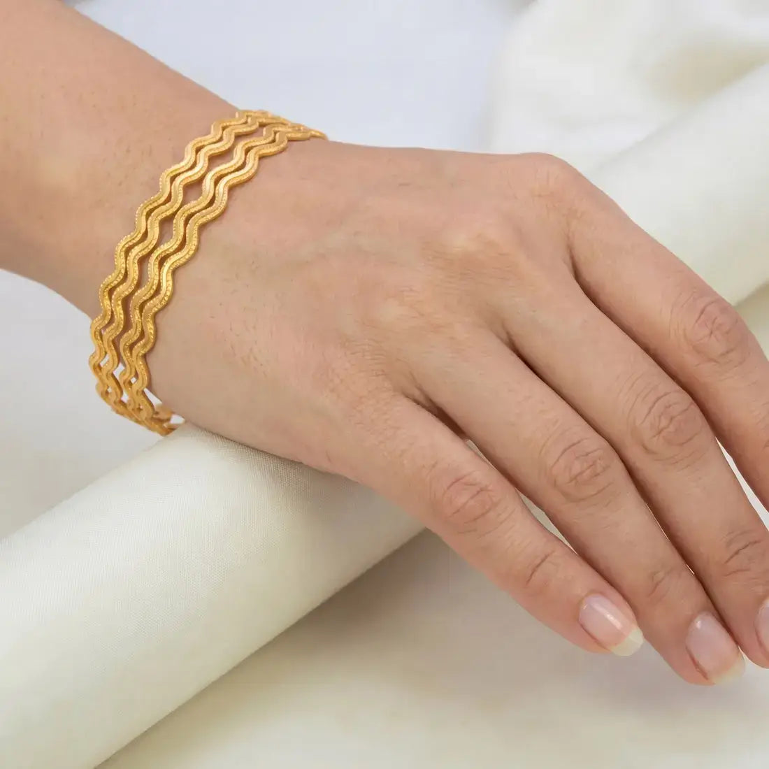 Hand wearing Unique Gold Plated Zigzag Bangles on a white background.
