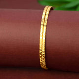 Trendy Gold-Plated Wavy Pattern Bangles displayed on a rich maroon surface, showcasing intricate gold designs.