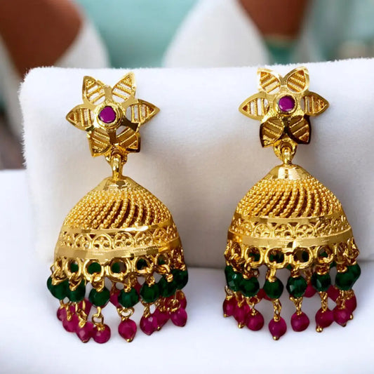 Gold earrings with red and green beads on a white cushion