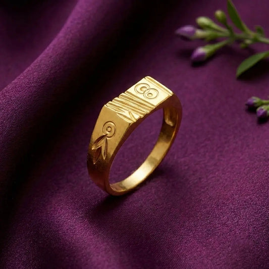 A gold ring with engraved tribal-style symbols, resting on a draped purple fabric background with small purple flowers in the corner.