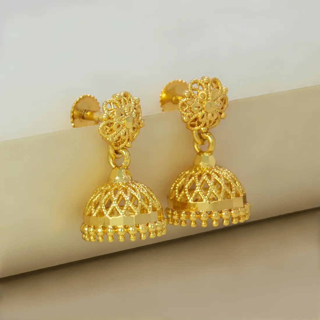 Gold plated earrings with intricate designs on a beige surface