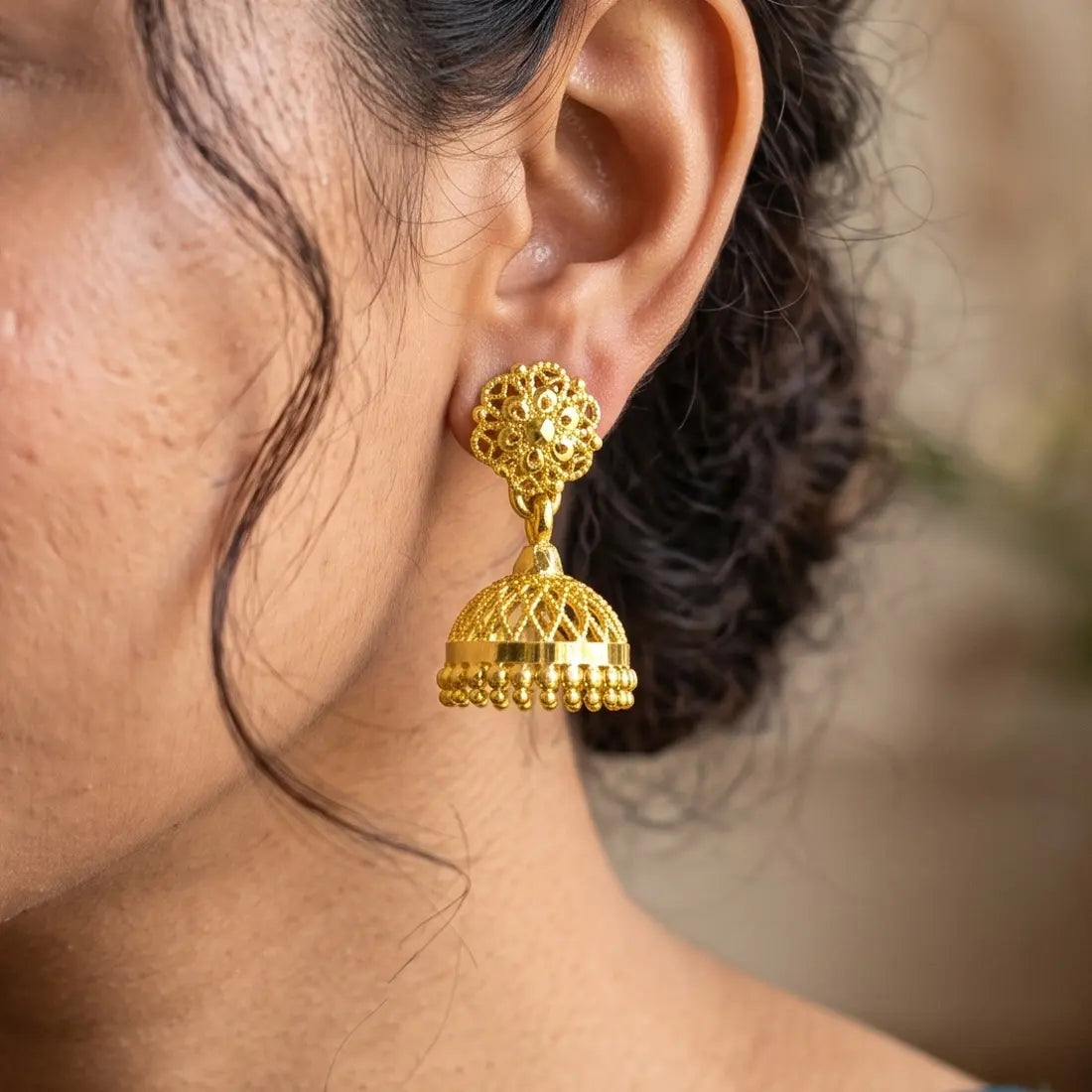 Close-up of a person wearing a gold plated jhumka earring with a blurred background